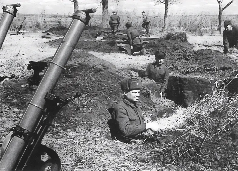 Freshly dug mounds of soil, bare bushes, and trees suggest that these mortar emplacements were being prepared during the spring of 1943. The mortars are the 82mm Model 1941. Two men moved these weapons on a two-wheeled carriage similar to a modern golf trolley; the wheels are just visible. The barrel is protected from the elements by a dust cap